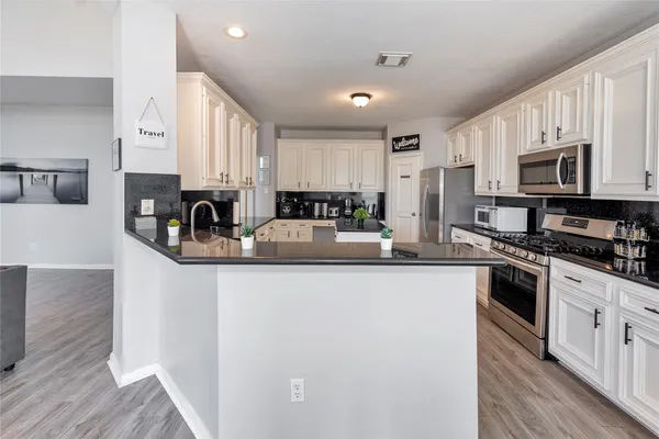 a kitchen with stainless steel appliances granite countertop a stove top oven a sink a refrigerator white cabinets and wooden floor