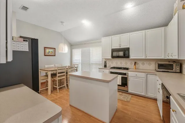 a kitchen with stainless steel appliances granite countertop a stove top oven a sink a refrigerator white cabinets and wooden floor