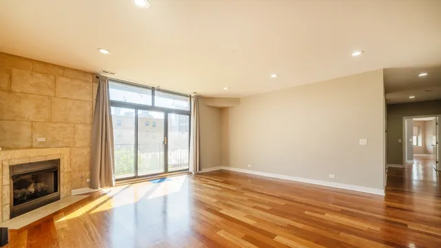 a view of an empty room with wooden floor fireplace and a window