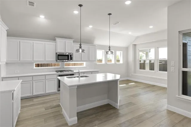 a kitchen with stainless steel appliances granite countertop a stove top oven a sink dishwasher a refrigerator and white cabinets with wooden floor