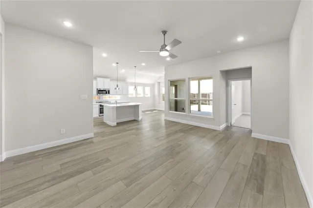an empty room with wooden floor and kitchen view