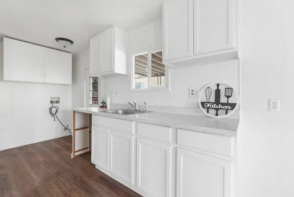 a kitchen with stainless steel appliances granite countertop a sink dishwasher a refrigerator and white cabinets with wooden floor