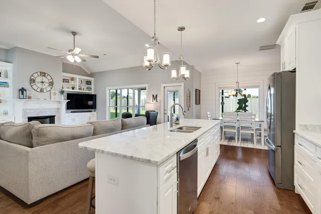 a large white kitchen with a stove a sink dishwasher a dining table and chairs with wooden floor