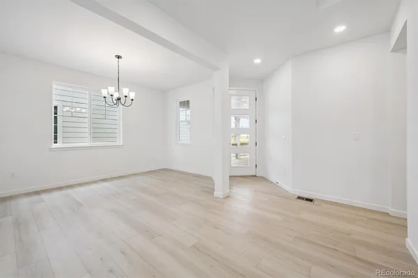 an empty room with wooden floor chandelier and windows