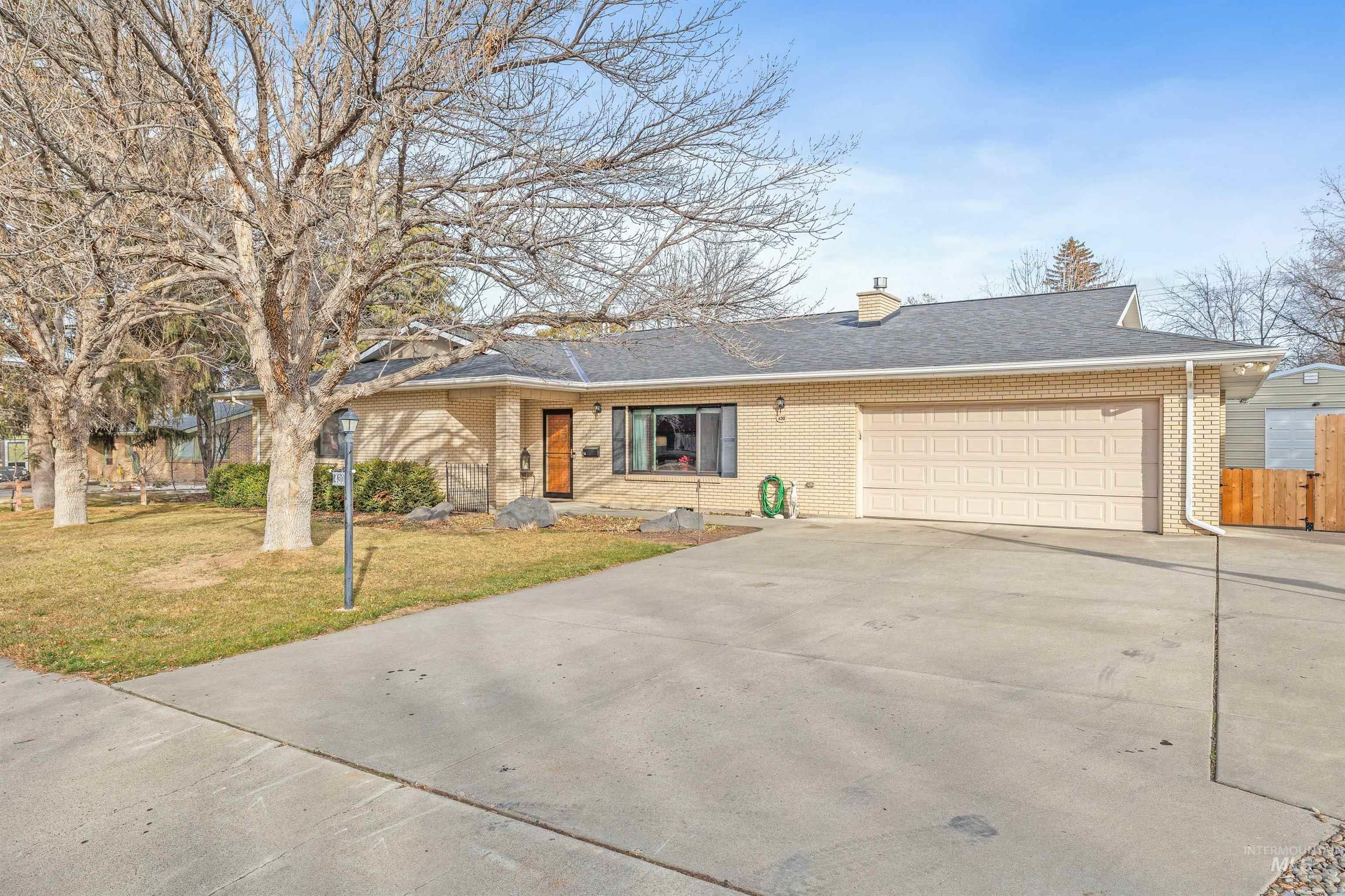 Single story home with driveway, brick siding, an attached garage, a chimney, and roof with shingles