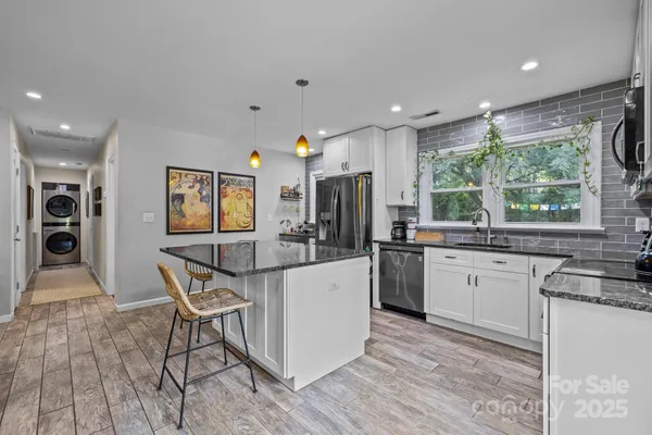 a kitchen with stainless steel appliances granite countertop a stove top oven a sink a refrigerator and white cabinets with wooden floor