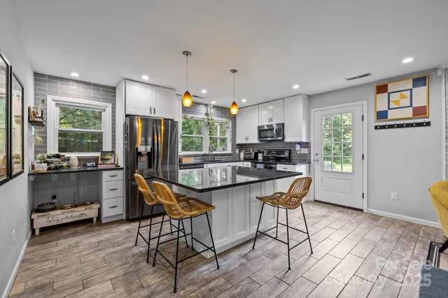 a kitchen with stainless steel appliances kitchen island granite countertop a refrigerator a stove a microwave oven a dining table and chairs with wooden floor
