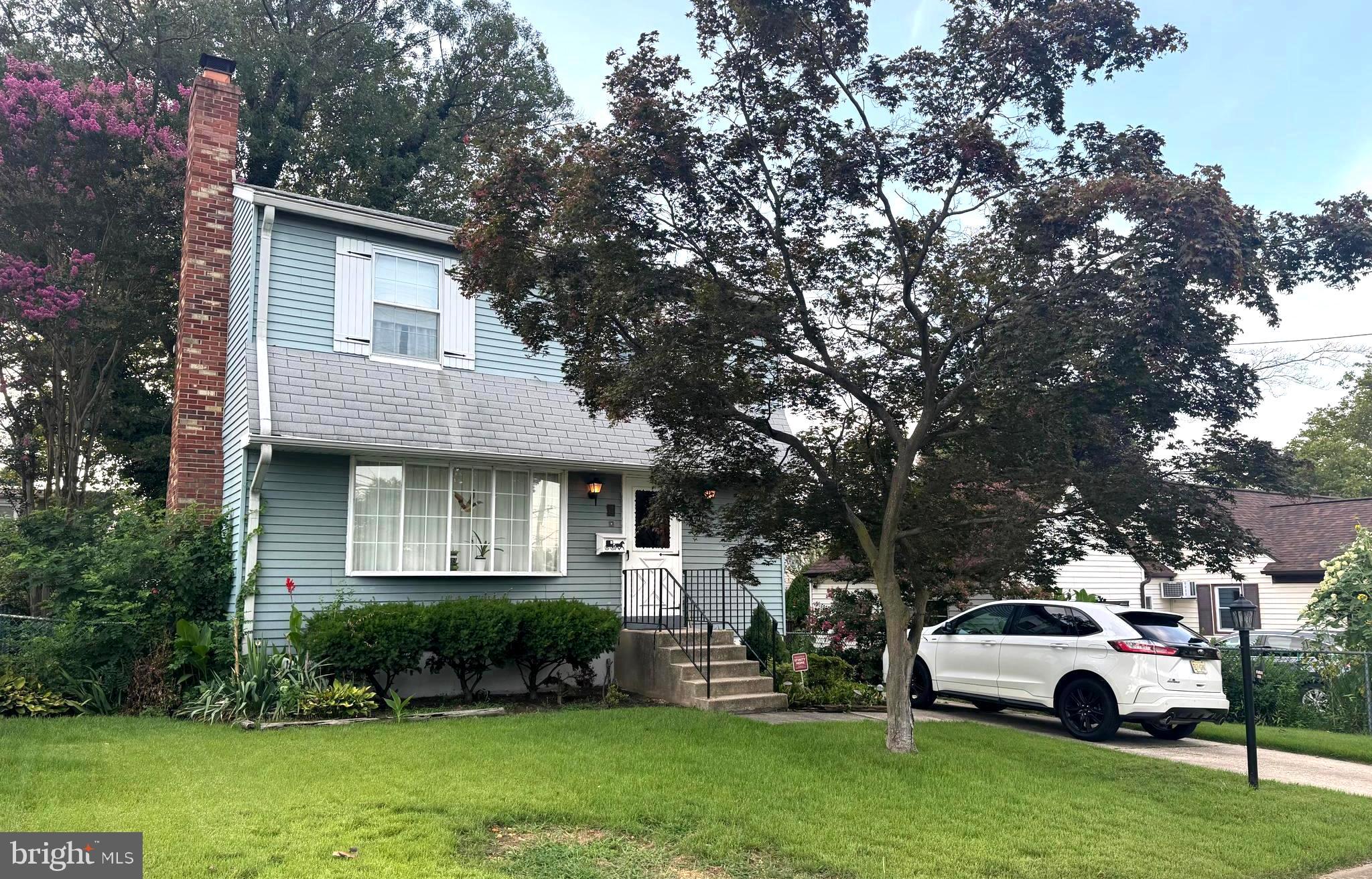 a white house in front of a yard with potted plants and large trees