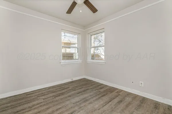 an empty room with wooden floor fan and windows