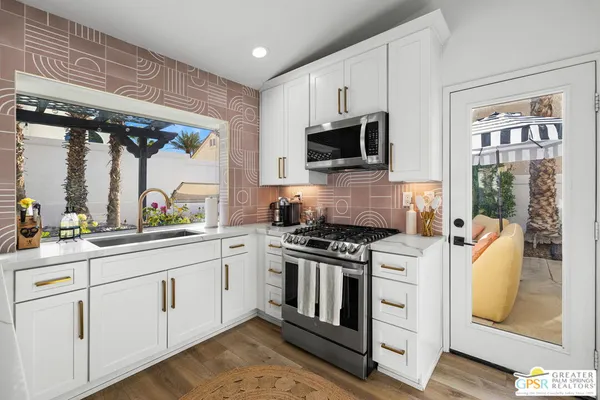 a large white kitchen with granite countertop a stove a sink a dining table and chairs with wooden floor