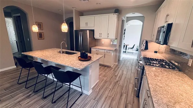 a kitchen with stainless steel appliances granite countertop a refrigerator a microwave a stove and white cabinets with wooden floor