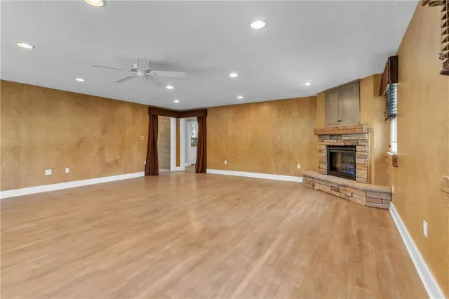 an empty room with wooden floor fireplace and windows