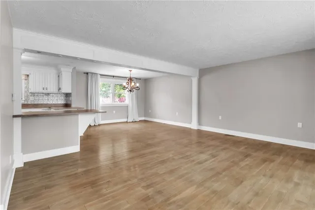 a view of empty room with wooden floor and kitchen view
