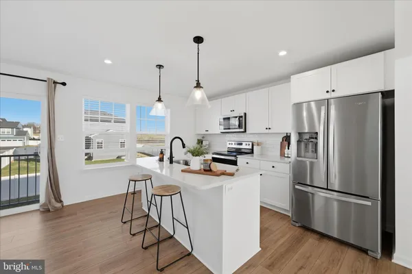 a kitchen with stainless steel appliances a stove a sink a refrigerator a center island and a wooden floor