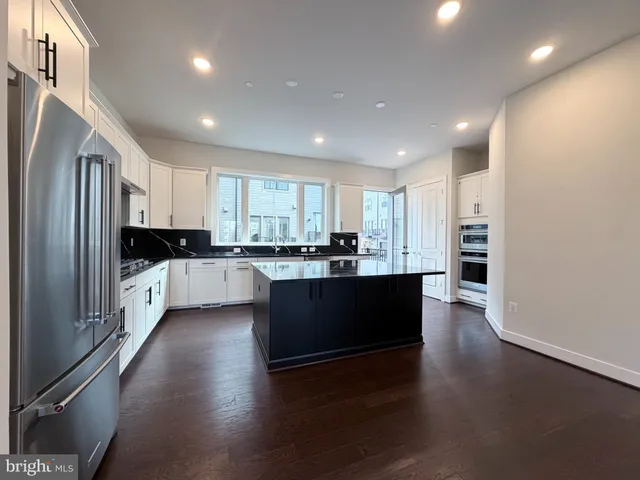 a large kitchen with stainless steel appliances granite countertop a refrigerator a sink dishwasher a stove and a refrigerator with wooden floor