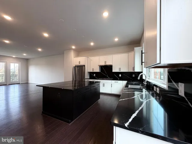 a view of kitchen with stainless steel appliances granite countertop a stove a sink a refrigerator and white cabinets with wooden floor