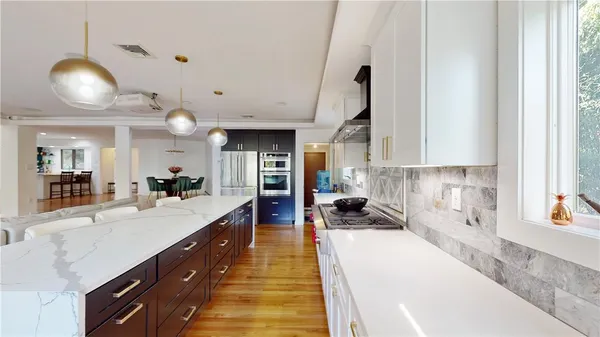 a large white kitchen with kitchen island a large counter space a sink a window and stainless steel appliances