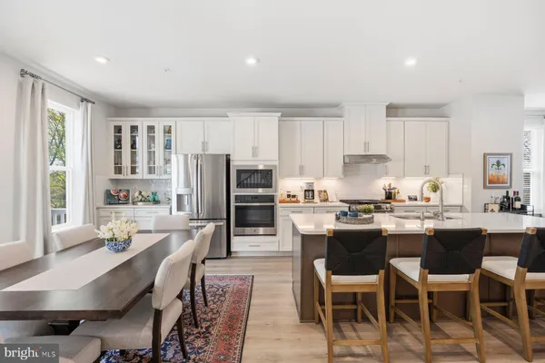 a dining area with stainless steel appliances kitchen island granite countertop a dining table chairs and a refrigerator