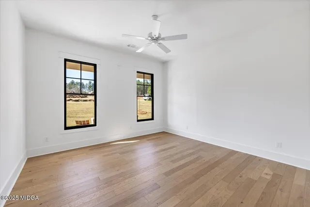 an empty room with wooden floor chandelier fan and windows