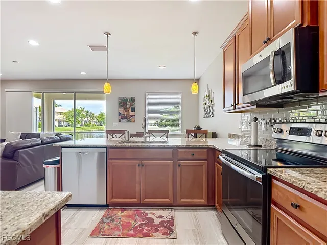 a kitchen with stainless steel appliances granite countertop wooden cabinets a sink dishwasher a stove and a refrigerator with wooden floor