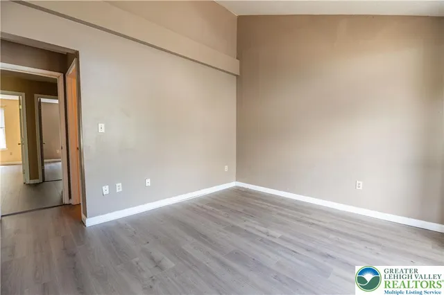 a view of an empty room with wooden floor and a ceiling fan