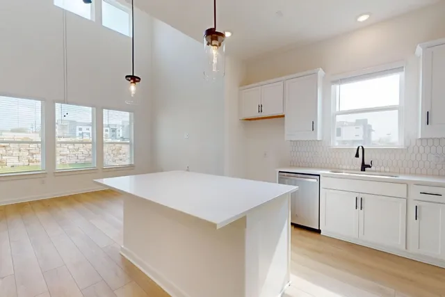 a kitchen with a stove a sink and white cabinets with wooden floor next to windows