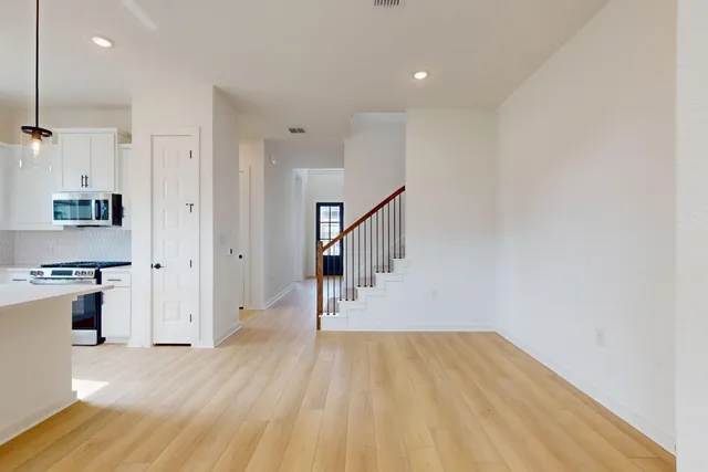 a view of empty room with wooden floor and kitchen