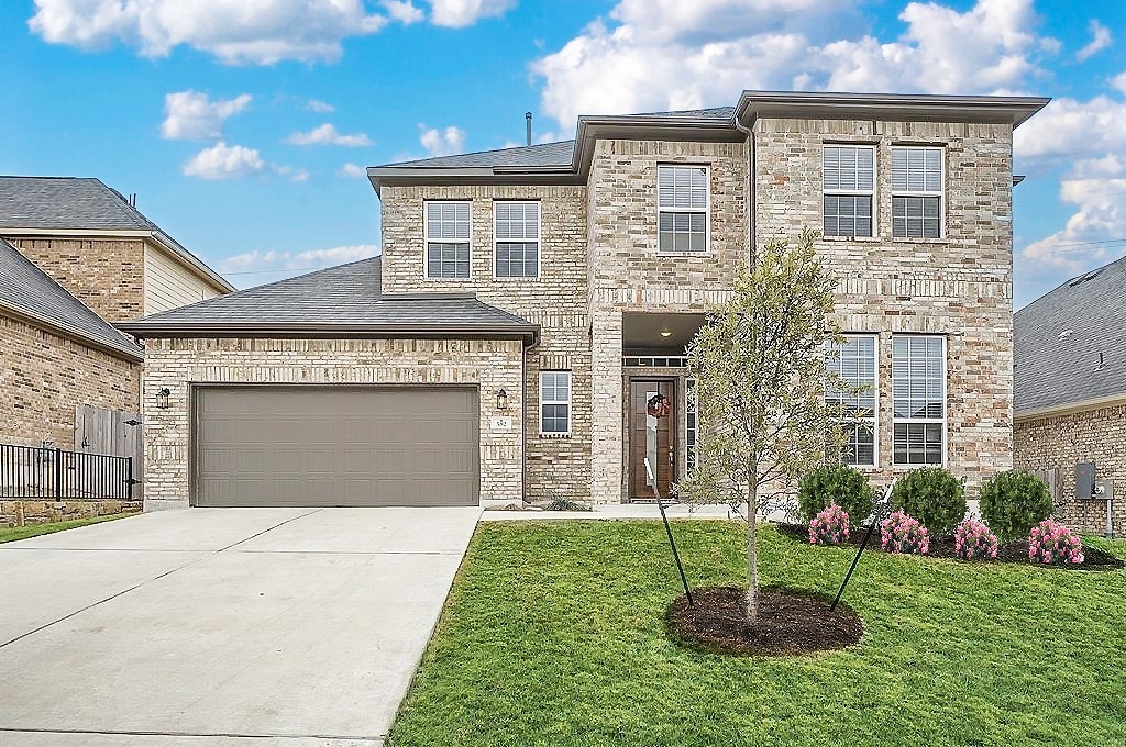 582 Wild Pecan Loop Buda, TX 78610 - Photo 26 of 28 View of front facade with concrete driveway, a front yard, brick siding, and a garage