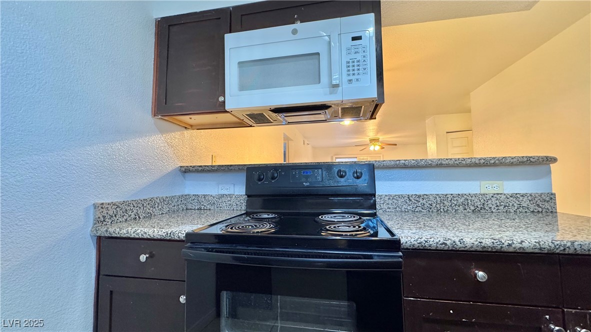2750 South Durango Drive, Unit 2100 Las Vegas, NV 89117 - Photo 13 of 30 Kitchen with black range with electric stovetop, white microwave, a textured wall, and light stone countertops
