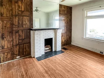 a view of an empty room with wooden floor fireplace and a window