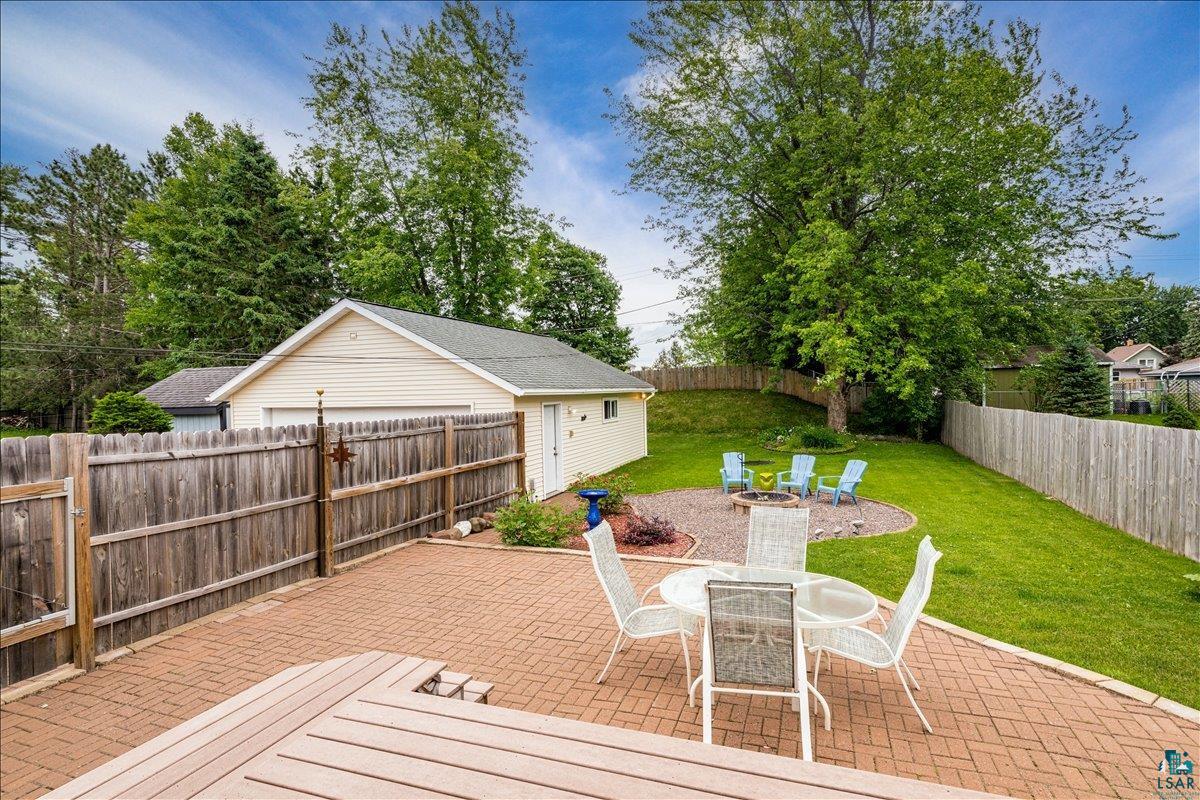 130 West Austin Street Duluth, MN 55803 - Photo 29 of 35 Expansive backyard featuring a brick paver patio, a dedicated fire pit area, a detached garage, and mature landscaping