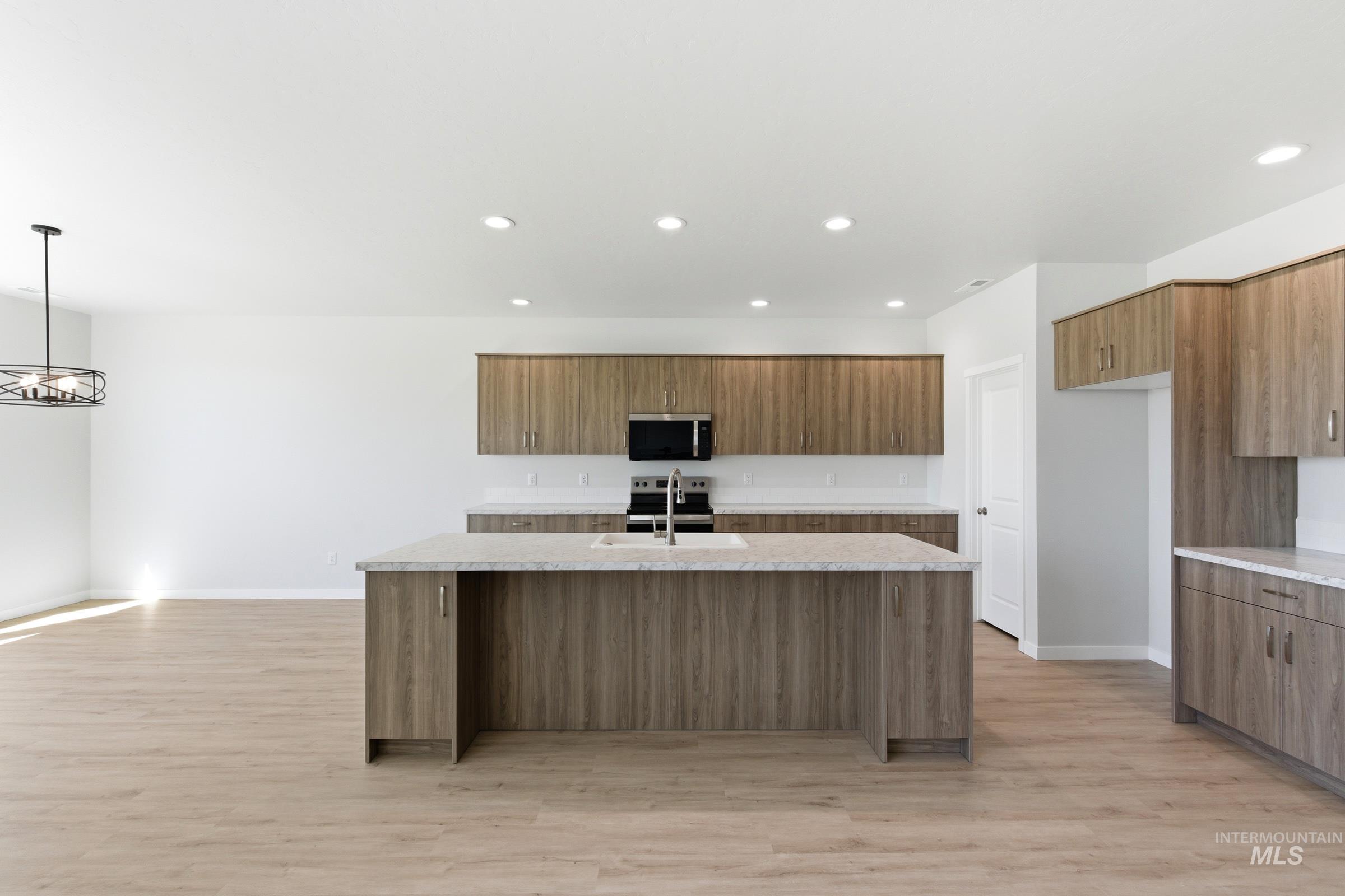 13663 Redway Court Caldwell, ID 83607 - Photo 3 of 32 Kitchen featuring a central island with an undermount sink, wood-finish cabinetry, light-toned countertops, and integrated stainless-steel appliances