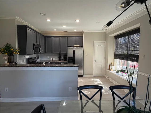 a kitchen with stainless steel appliances granite countertop a refrigerator a stove a sink and a dining table with white cabinets