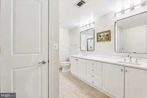 a spacious bathroom with a double vanity sink a mirror and a toilet
