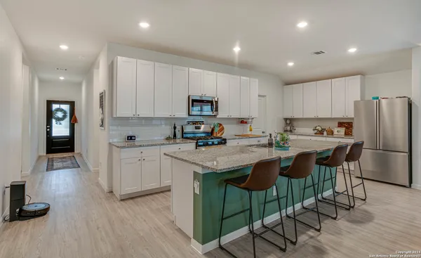 a kitchen with granite countertop a refrigerator a stove a sink a dining table and chairs with wooden floor