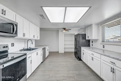 a kitchen with stainless steel appliances granite countertop white cabinets a sink a stove a refrigerator with grey cabinets