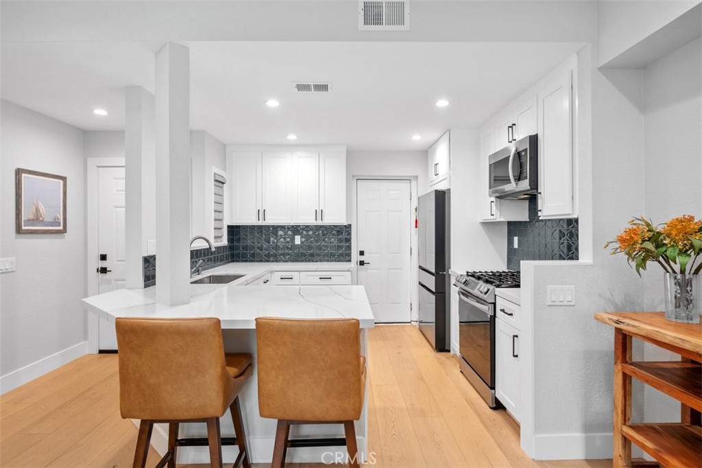 26 Sunbridge Place Dana Point, CA 92629 - Photo 2 of 15 a large white kitchen with stainless steel appliances granite countertop a stove a sink a refrigerator and a dining table with wooden floor