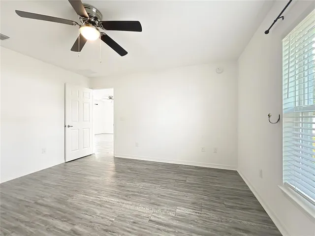 an empty room with wooden floor fan and windows