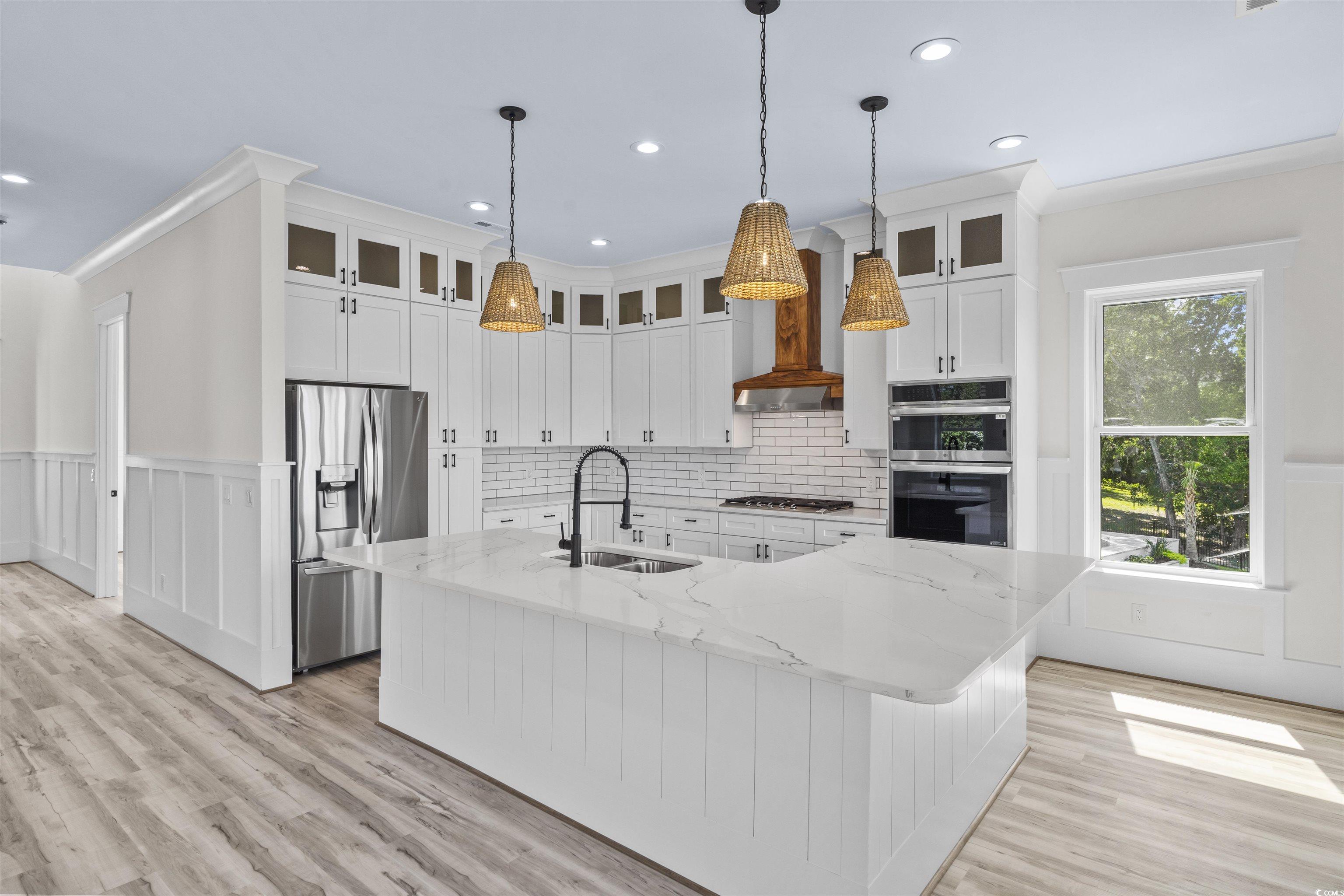 1017 Hyatt Pond Road North Myrtle Beach, SC 29582 - Photo 4 of 39 Kitchen featuring stainless steel appliances, a wainscoted wall, white cabinets, a spacious island, and light wood-style flooring