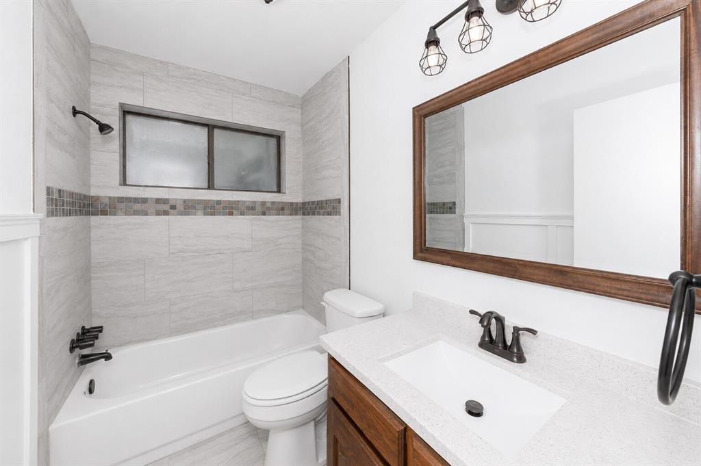 1001 Rosebud Drive Azle, TX 76020 - Photo 7 of 36 Bathroom featuring a white bathtub, light-toned tile surround with decorative accent band, bronze-finish fixtures, wood-tone vanity with a light countertop, and a large framed mirror