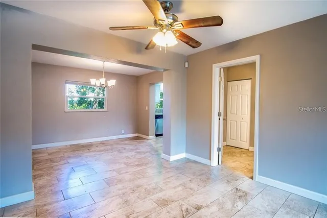 a view of an empty room with window and chandelier fan