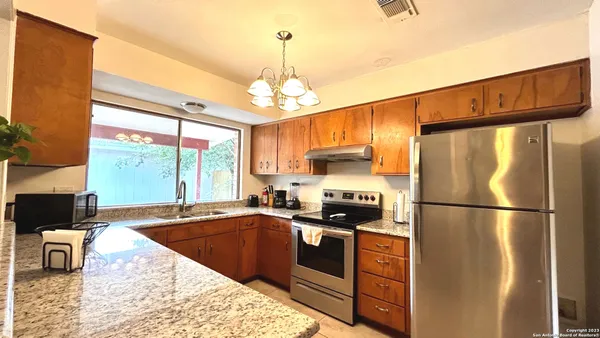 a kitchen with stainless steel appliances granite countertop a refrigerator a sink dishwasher a stove and a dining table with wooden floor
