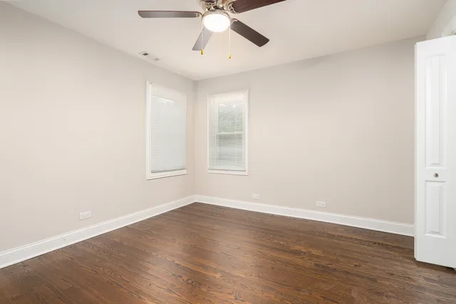 a view of an empty room with wooden floor and a ceiling fan