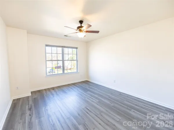 an empty room with wooden floor chandelier fan and windows