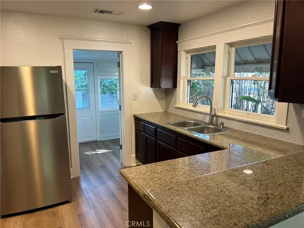 a kitchen with granite countertop a refrigerator a sink and wooden floors