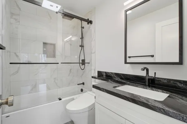 a bathroom with a granite countertop sink a toilet a mirror a bathtub and shower
