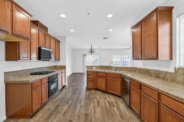 a kitchen with stainless steel appliances granite countertop wooden cabinets a sink dishwasher a stove and a refrigerator with wooden floor