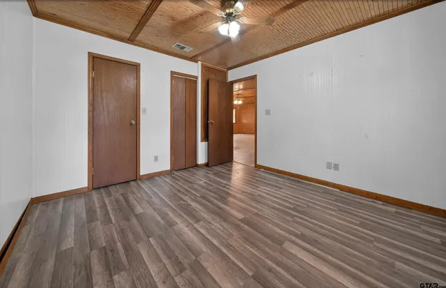 a view of an empty room with wooden floor and a ceiling fan