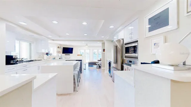 a large white kitchen with stainless steel appliances kitchen island a stove a oven a sink dishwasher and white cabinets with wooden floor