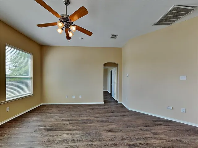 an empty room with wooden floor chandelier fan and windows